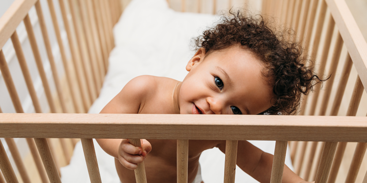 An adorable baby standing. in their crib and smiling at the viewer