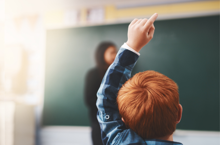 A little redhead boy raising his hand in class