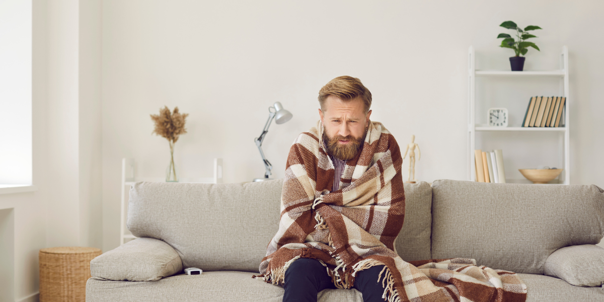 a cold man wrapping himself in a blanket while on his couch